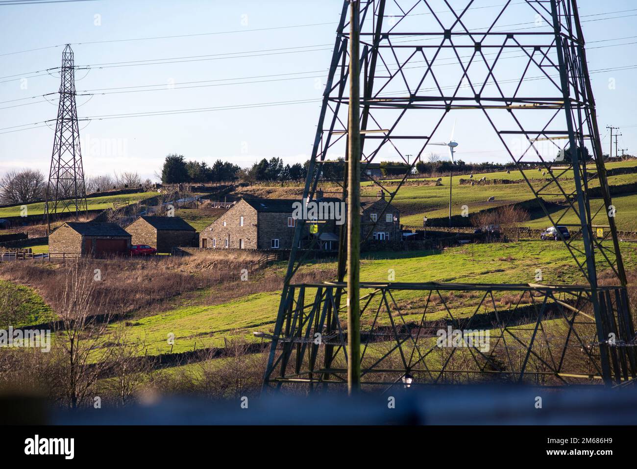 Strommasten und Windturbinen in der Pennine-Landschaft rund um Queensbury und Calderdale, West Yorkshire, Großbritannien, an einem Tag im Januar im Norden Englands, an dem der blaue Himmel erstrahlt. Kredit: Windmill Images/Alamy Live News Stockfoto