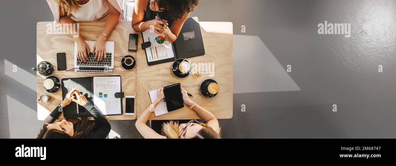 Teamarbeit in einem kleinen Unternehmensteam aus Unternehmerinnen diskutiert Startup-Ideen. Draufsicht von vier Frauen, die am Tisch sitzen, im Café mit Laptop, Graben Stockfoto