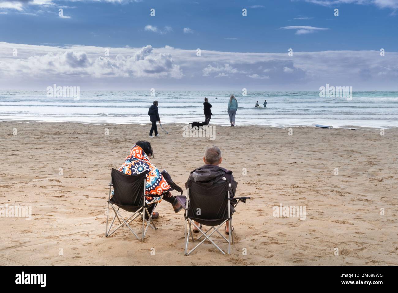 Zwei Urlauber sitzen auf Klappstühlen am Fistral Beach und blicken auf das Meer in Newquay in Cornwall in England. Stockfoto