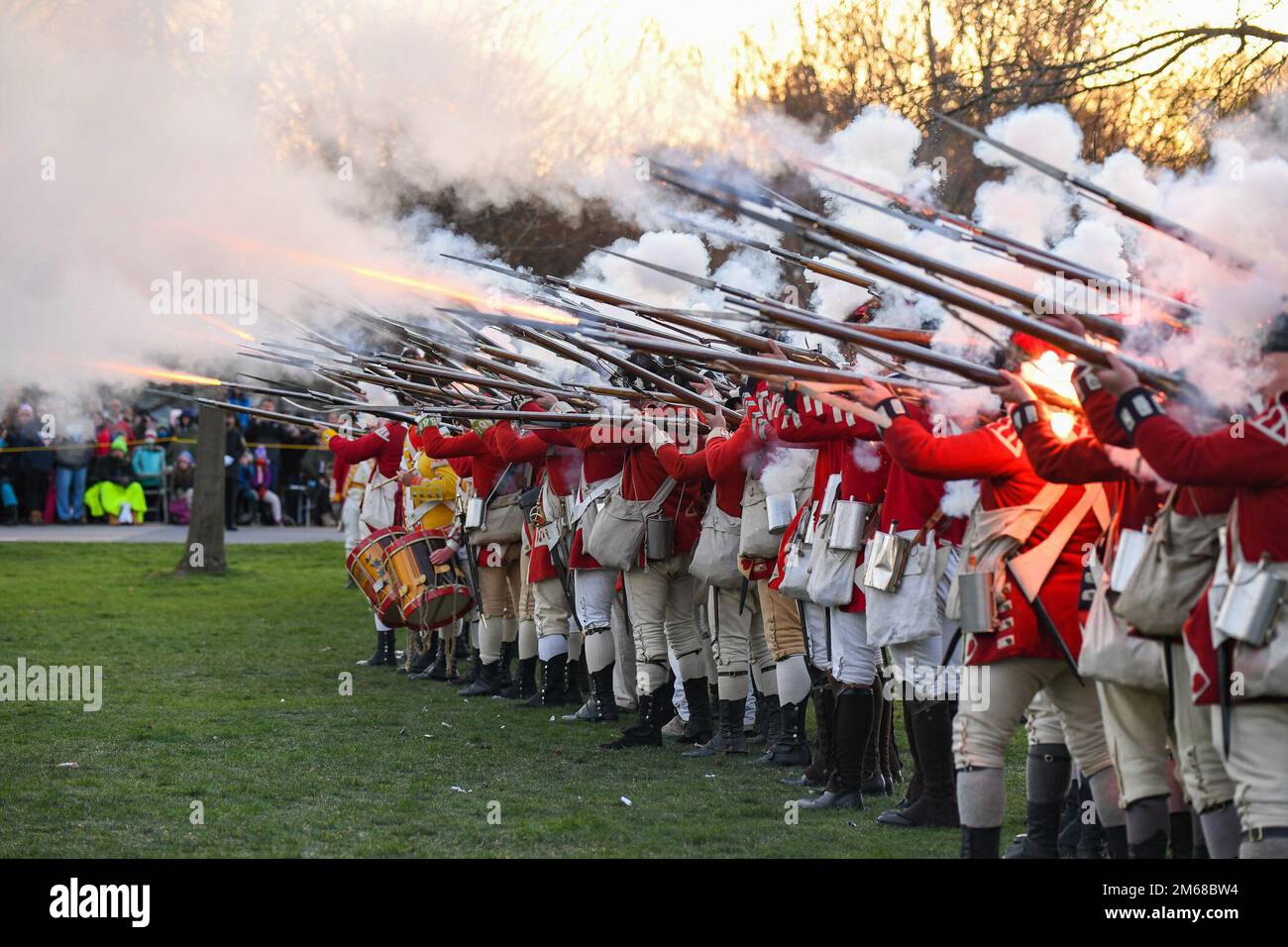 Britische Regulars feuern Musketen während einer Nachstellung des Patriots' Day in Lexington, Mass., April 18. Der Patriots' Day ist ein besonderer Feiertag in Massachusetts, an dem die Eröffnungsschlacht des Amerikanischen Unabhängigkeitskriegs am 19. April 1775 gedenkt wird. Stockfoto