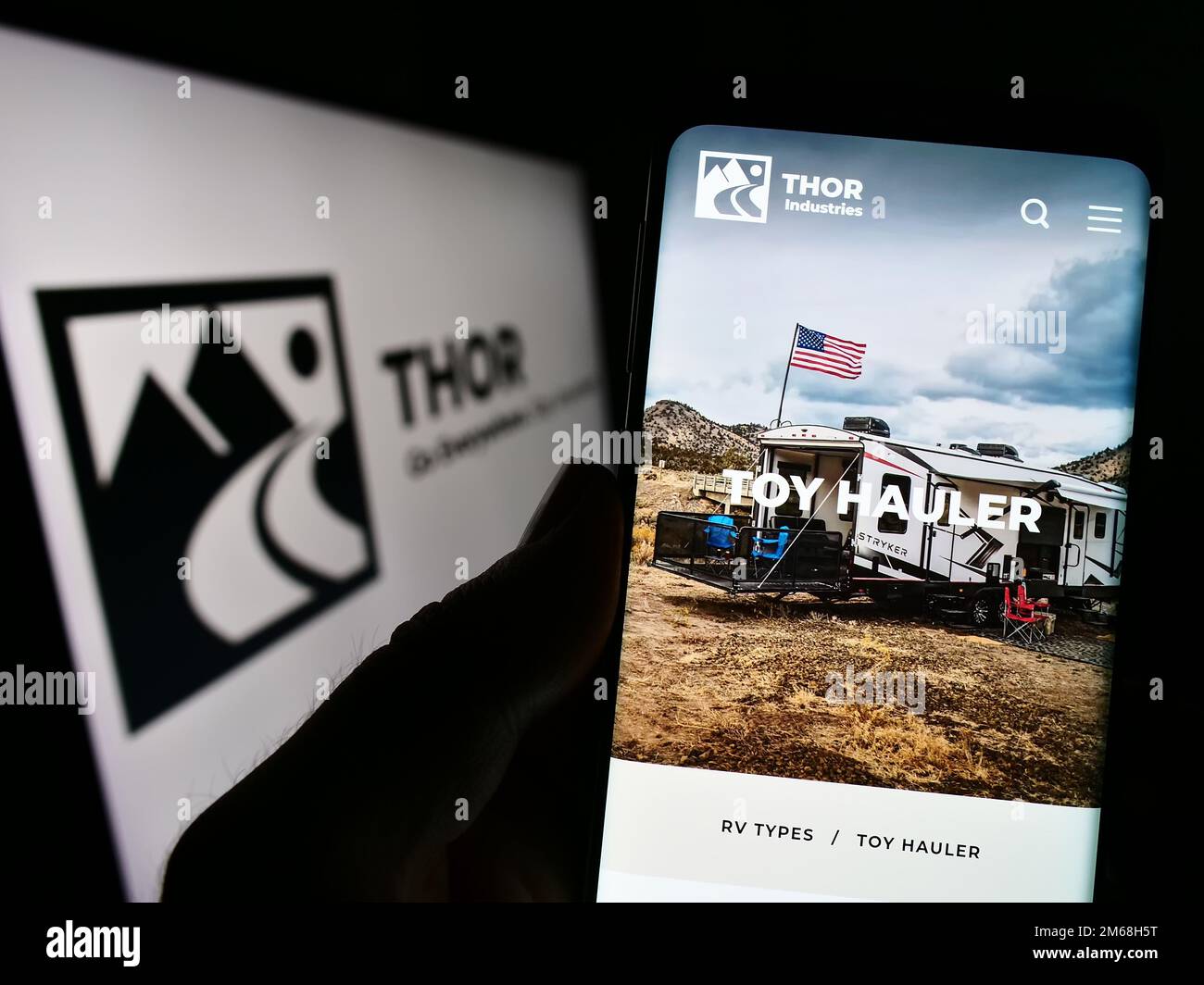 Person, die ein Mobiltelefon mit einer Webseite des US-amerikanischen RV-Herstellers Thor Industries Inc. Auf dem Bildschirm mit Logo hält. Konzentrieren Sie sich auf die Mitte des Telefondisplays. Stockfoto