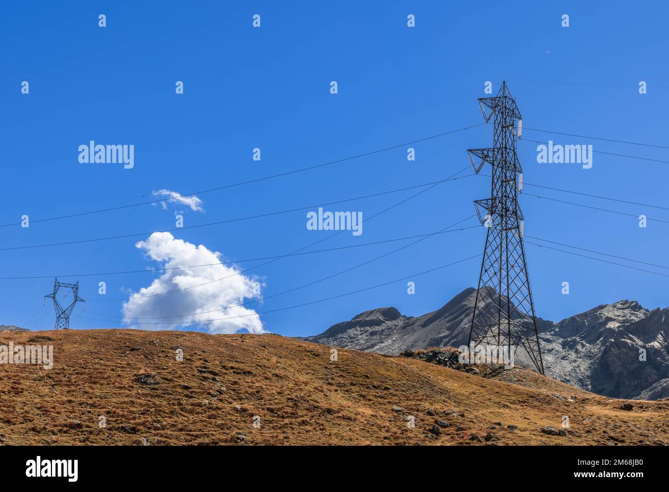 Hochspannungsleitungen verlegen entlang der Granitabhänge mit verwelktem Herbstgras vor dem Hintergrund eines klaren blauen Himmels Stockfoto