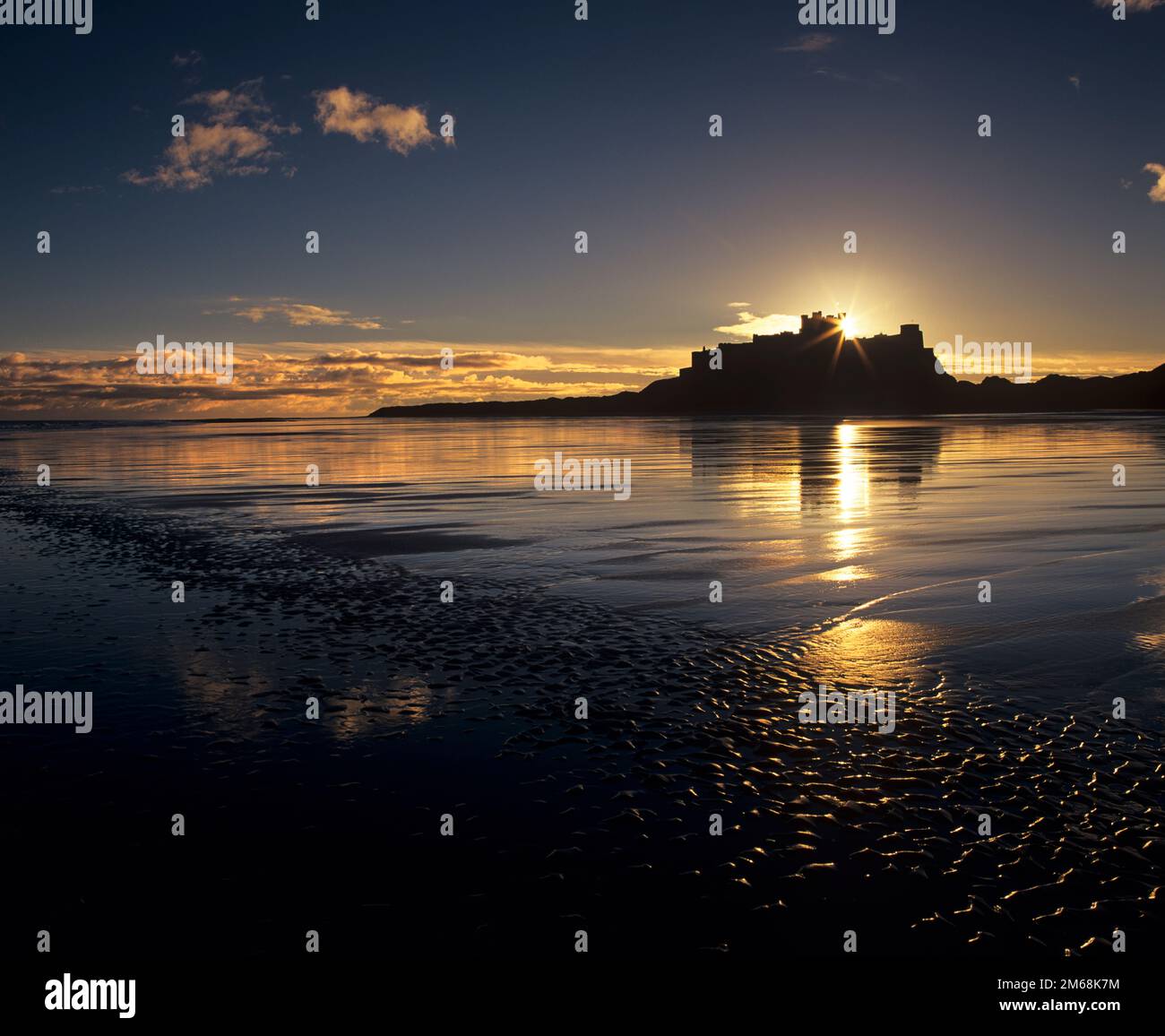 Hinter Bamburgh Castle und dem Strand in Northumberland, England, geht eine goldene Sonne auf Stockfoto