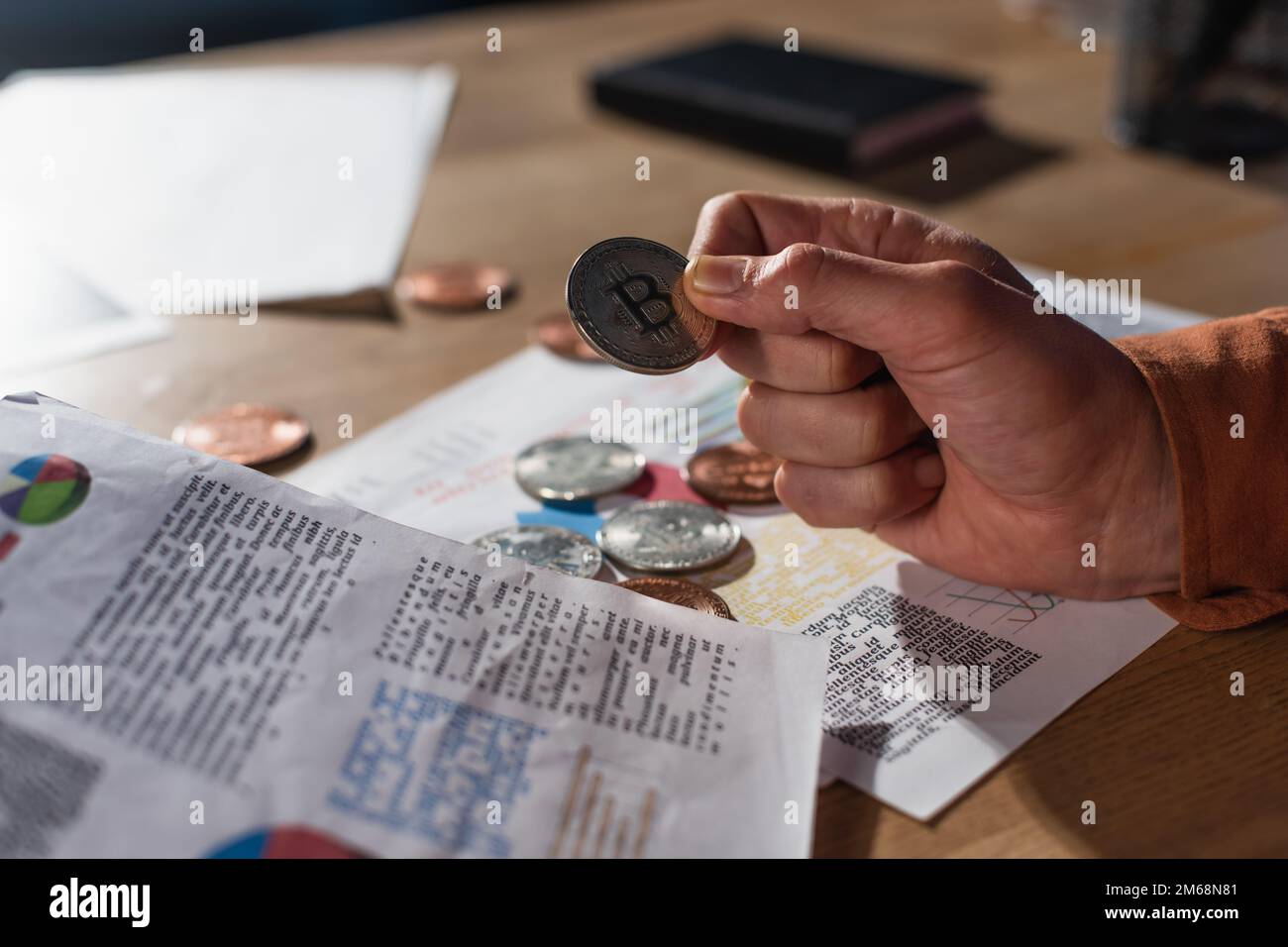 KIEW, UKRAINE - 17. NOVEMBER 2022: Silberbitmünze in der Hand eines verkürzten Geschäftsmannes, fast verschwommene Papiere mit Grafiken Stockfoto