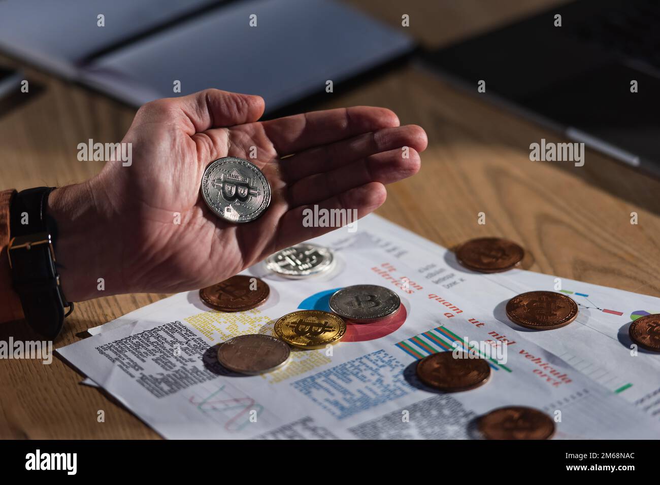 KIEW, UKRAINE - 17. NOVEMBER 2022: Silberne Bitcoin in der Hand eines gekürzten Mannes in der Nähe von Papieren mit Geschäftsanalysen Stockfoto