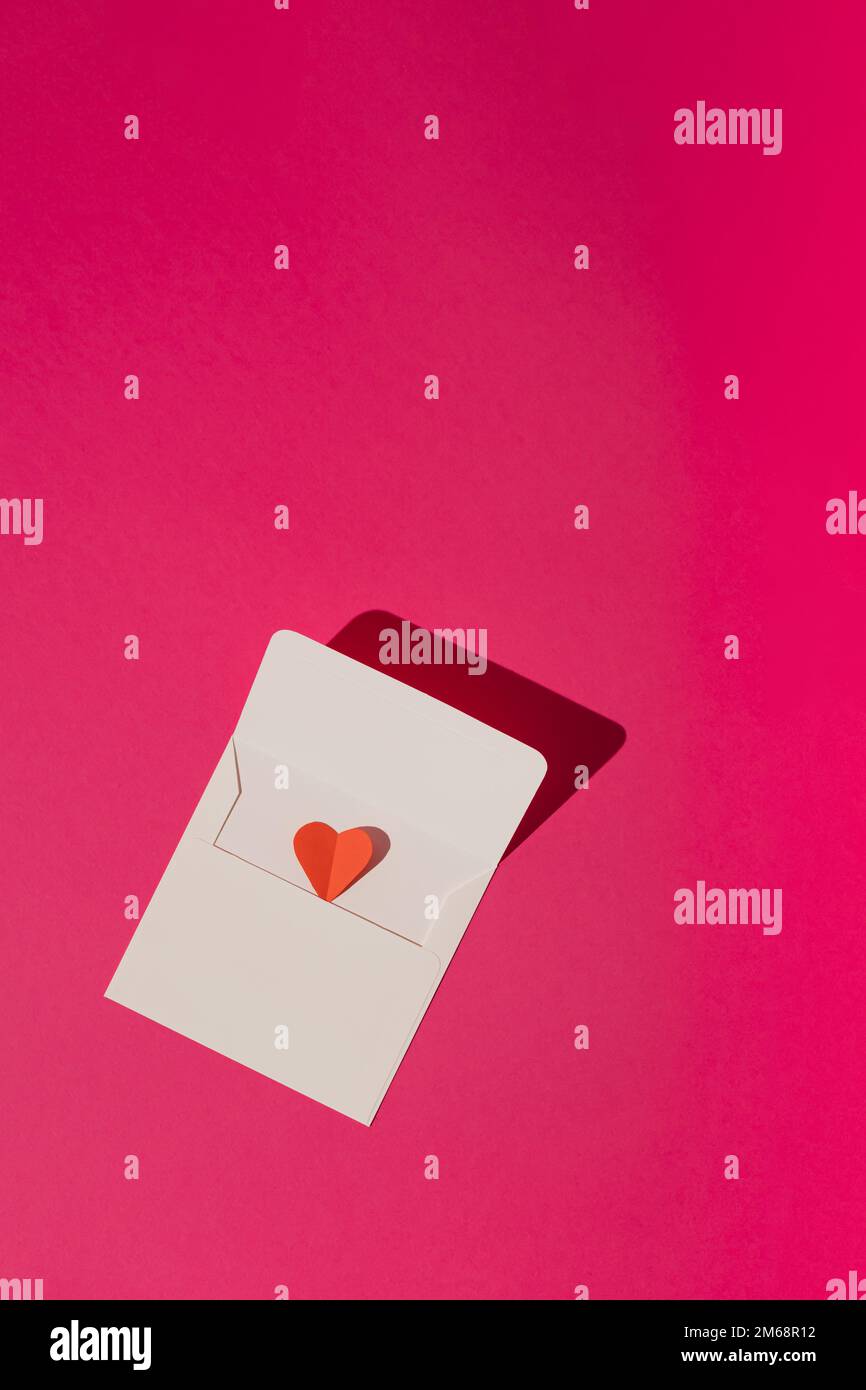 Weißer Umschlag mit rotem Herz auf magentarosa-rosa Hintergrund. Minimale Liebe oder valentinskonzept. Stockfoto