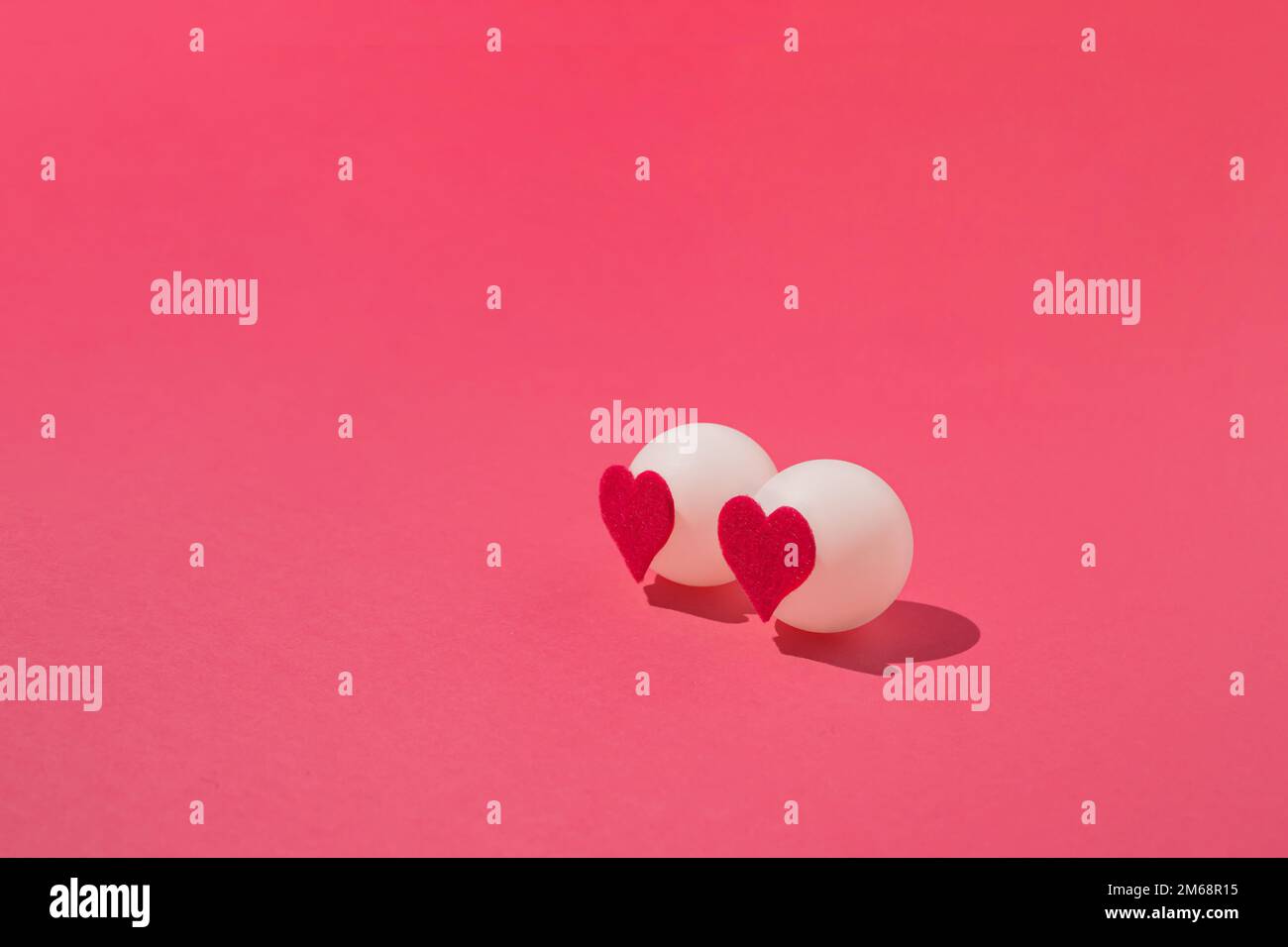 Zwei weiße Pingbälle mit Filzherzen auf pinkfarbenem Hintergrund. Minimale Liebe oder valentinskonzept. Stockfoto