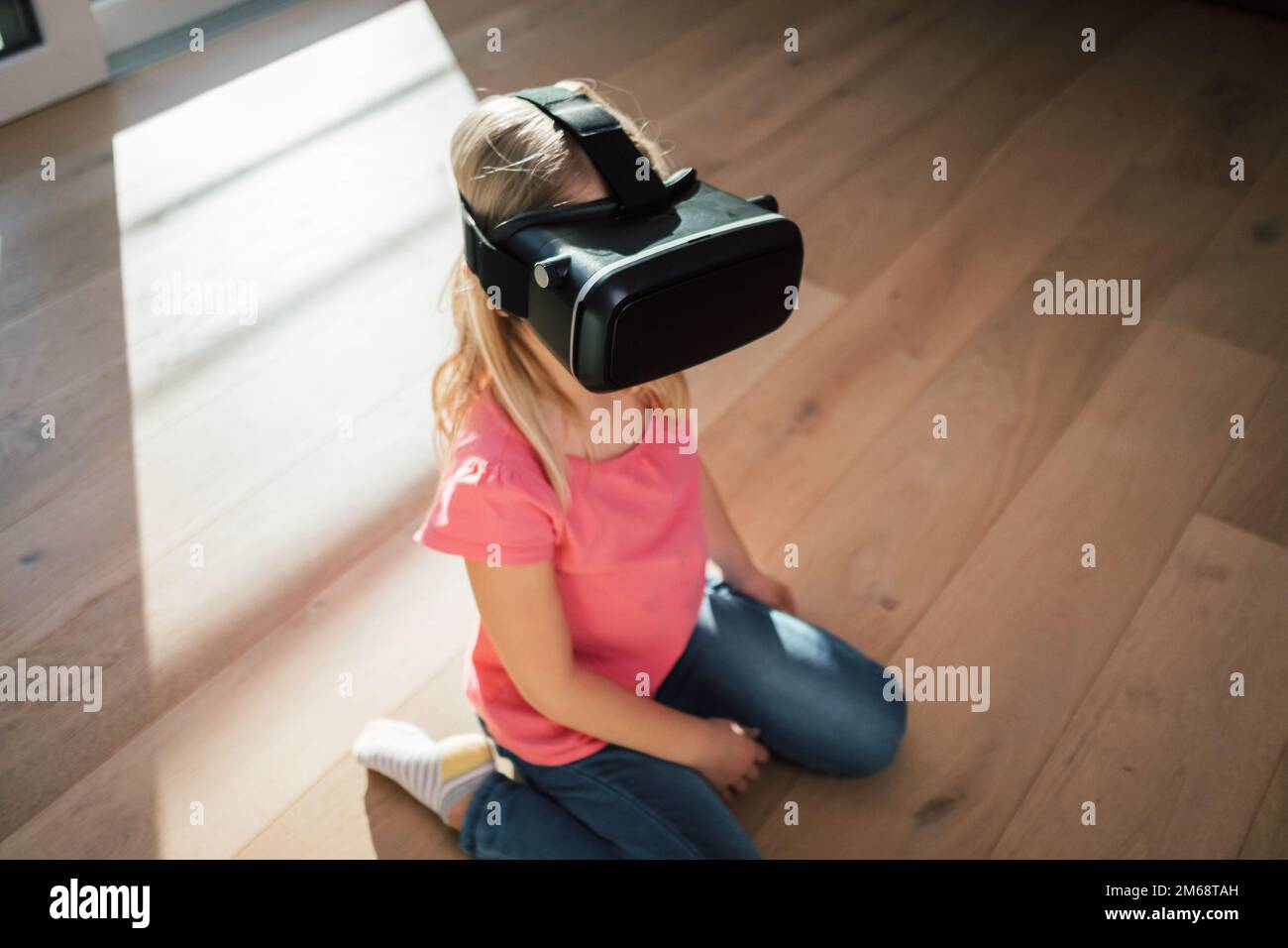 Kaukasische Frau in einem Virtual-Reality-Headset, die auf dem Boden des Wohnzimmers sitzt und sich auf die virtuelle Welt freut Stockfoto