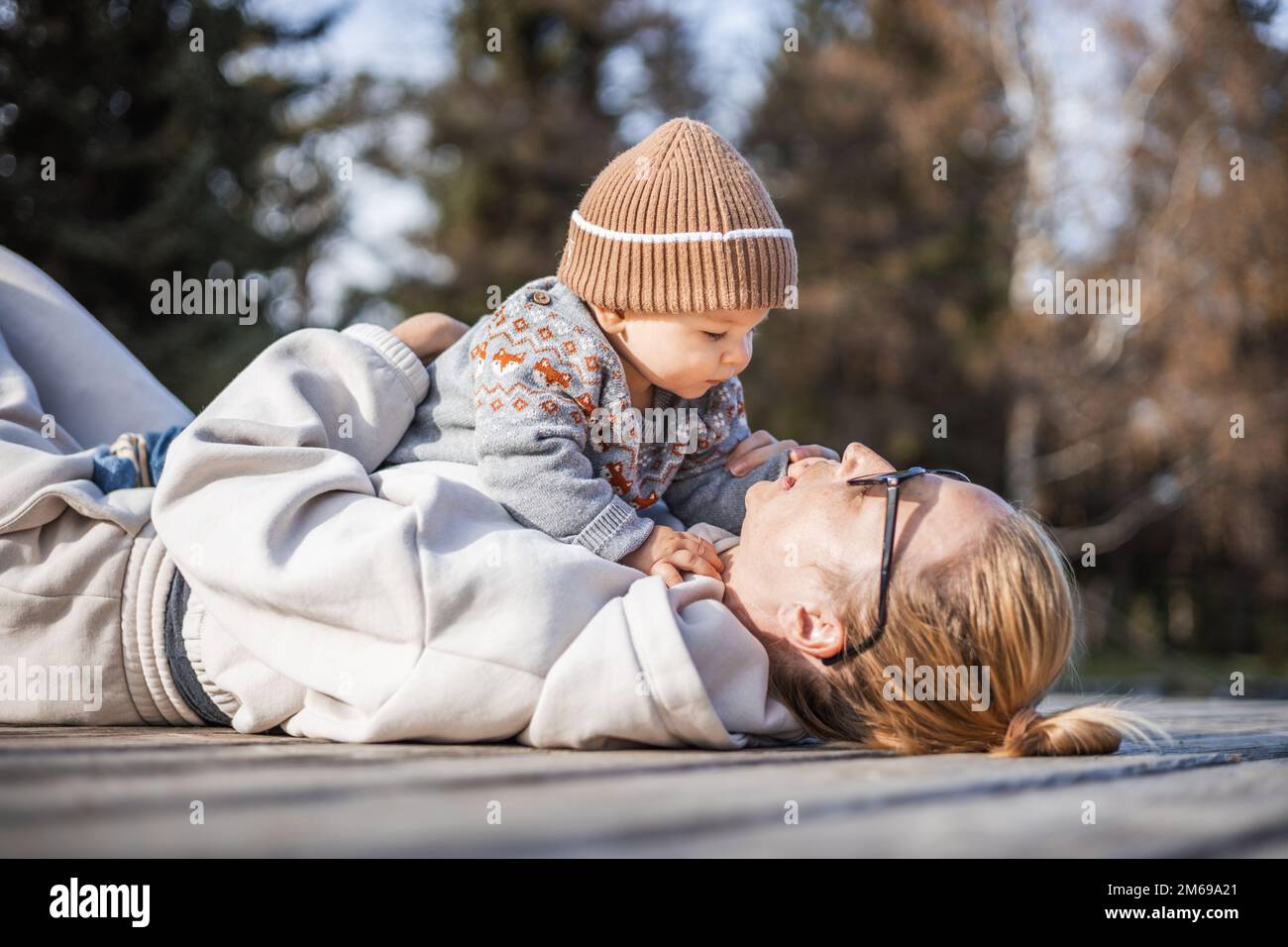 Glückliche Familie. Junge Mutter, die mit ihrem kleinen Jungen an einem sonnigen Herbsttag außerhalb der Tür spielt. Porträt von mutter und Sohn auf einer hölzernen Plattform am See. Positive menschliche Emotionen, Gefühle, Freude Stockfoto