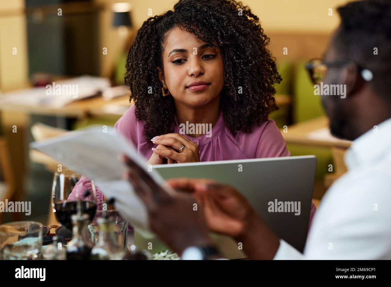 Eine fokussierte Geschäftsfrau sitzt mit ihrem Kollegen in einem Restaurant und hört sich Ratschläge für ein Start-up-Unternehmen an. Stockfoto