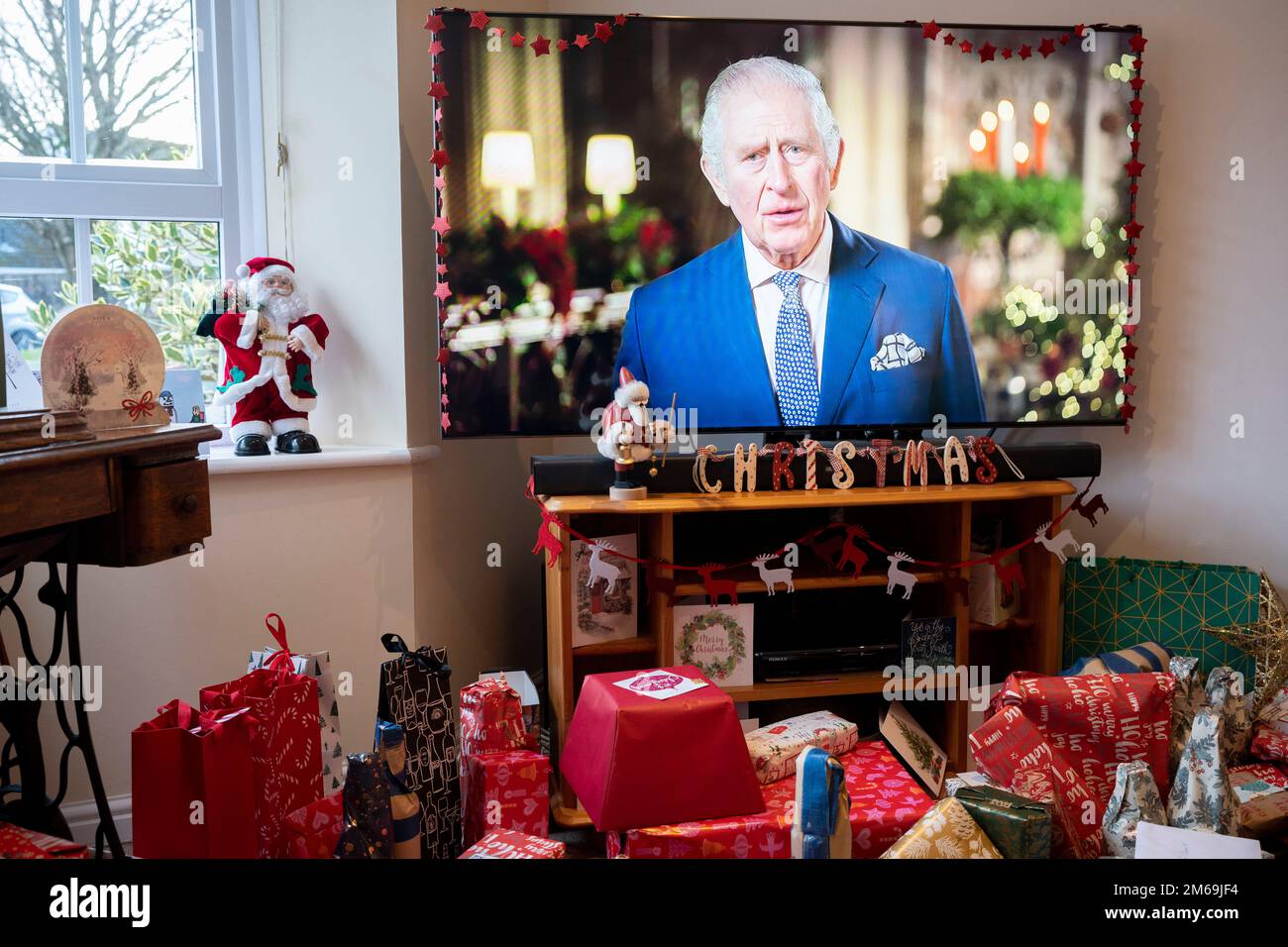 An seiner ersten Weihnachtssendung an die Nation seit dem Tod seiner Mutter, Königin Elizabeth III. Im September, spricht König Karl III. Mit einer Vorstadtfamilie auf ihrem Breitbild-TV in ihrem Wohnzimmer, das mit Geschenken gefüllt ist, am 25. Dezember 2022 in Nailsea, England. Stockfoto