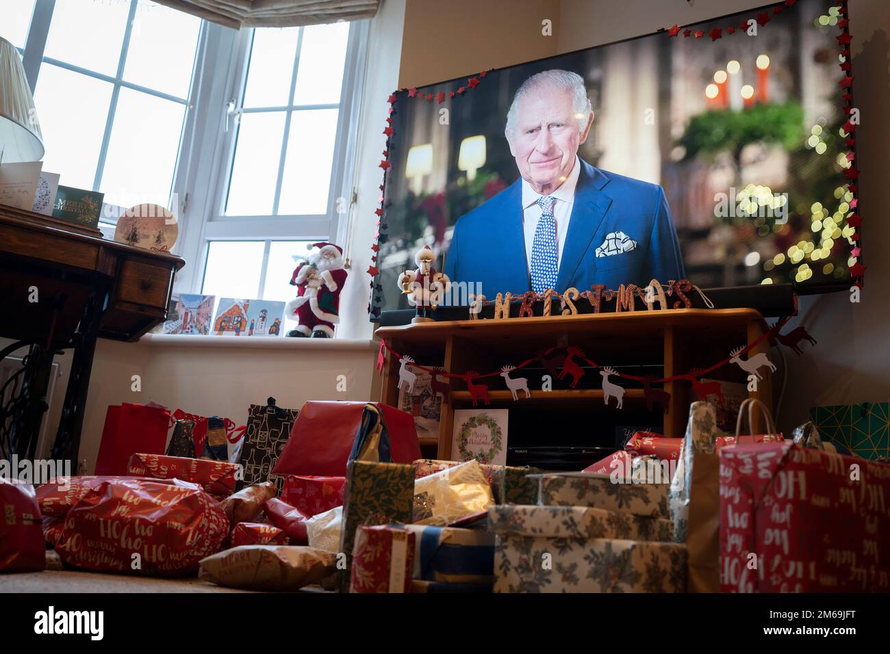 An seiner ersten Weihnachtssendung an die Nation seit dem Tod seiner Mutter, Königin Elizabeth III. Im September, spricht König Karl III. Mit einer Vorstadtfamilie auf ihrem Breitbild-TV in ihrem Wohnzimmer, das mit Geschenken gefüllt ist, am 25. Dezember 2022 in Nailsea, England. Stockfoto