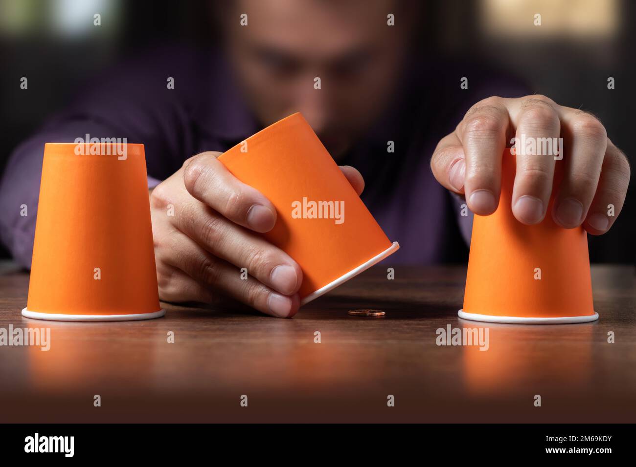 Der Mann zeigt ein Hütchenspiel von Fingern mit Münzen und dunklem Hintergrund. Konzepttäuschung, schlaue Hand Stockfoto