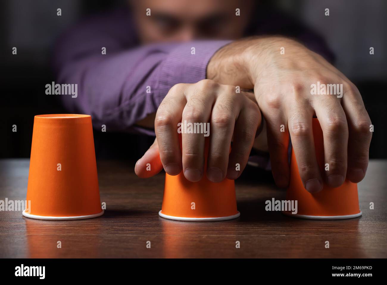 Der Mann zeigt ein Hütchenspiel von Fingern mit Münzen und dunklem Hintergrund. Konzepttäuschung, schlaue Hand Stockfoto