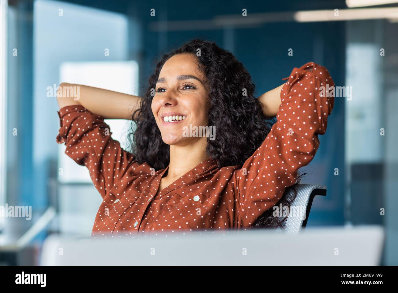 Glückliche und lächelnde erfolgreiche hispanische Geschäftsfrau beendete Arbeit zufrieden mit Arbeitsergebnis und Leistung, Hände hinter dem Kopf und lächelnd aus nächster Nähe. Stockfoto