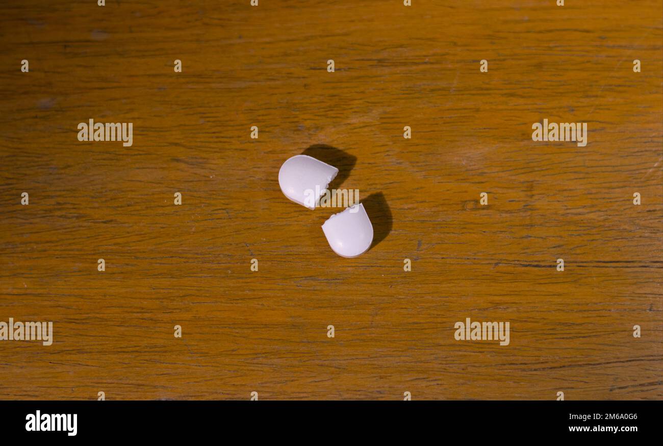 Eine zerbrochene weiße Pille oder Tablette auf einem Holztisch. Schließen Stockfoto