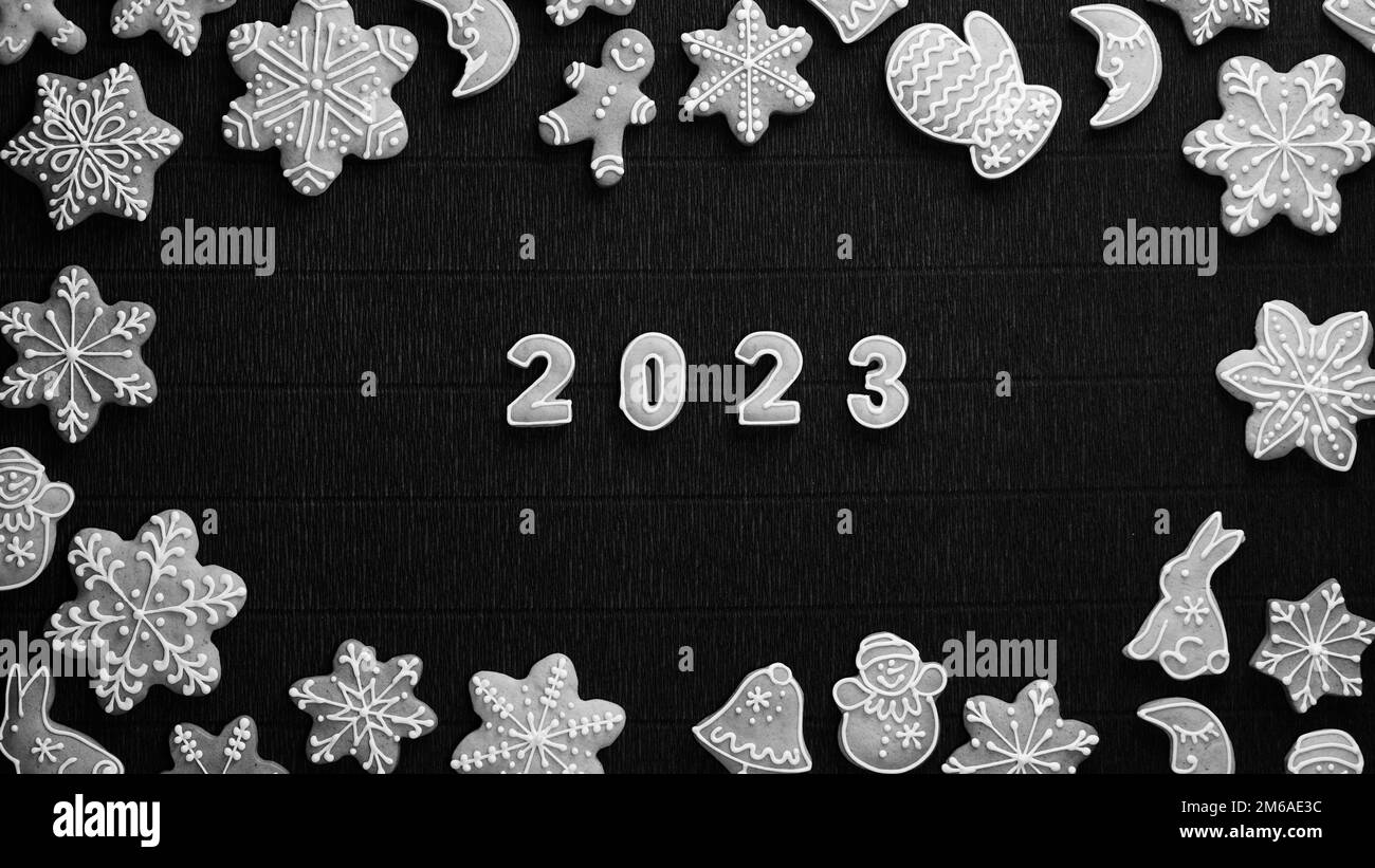 Weihnachtsrand mit glasierten Keksen mit Datum 2023 auf dunklem Hintergrund. Blick von oben. Frohes neues Jahr. Schwarz auf Weiß Stockfoto
