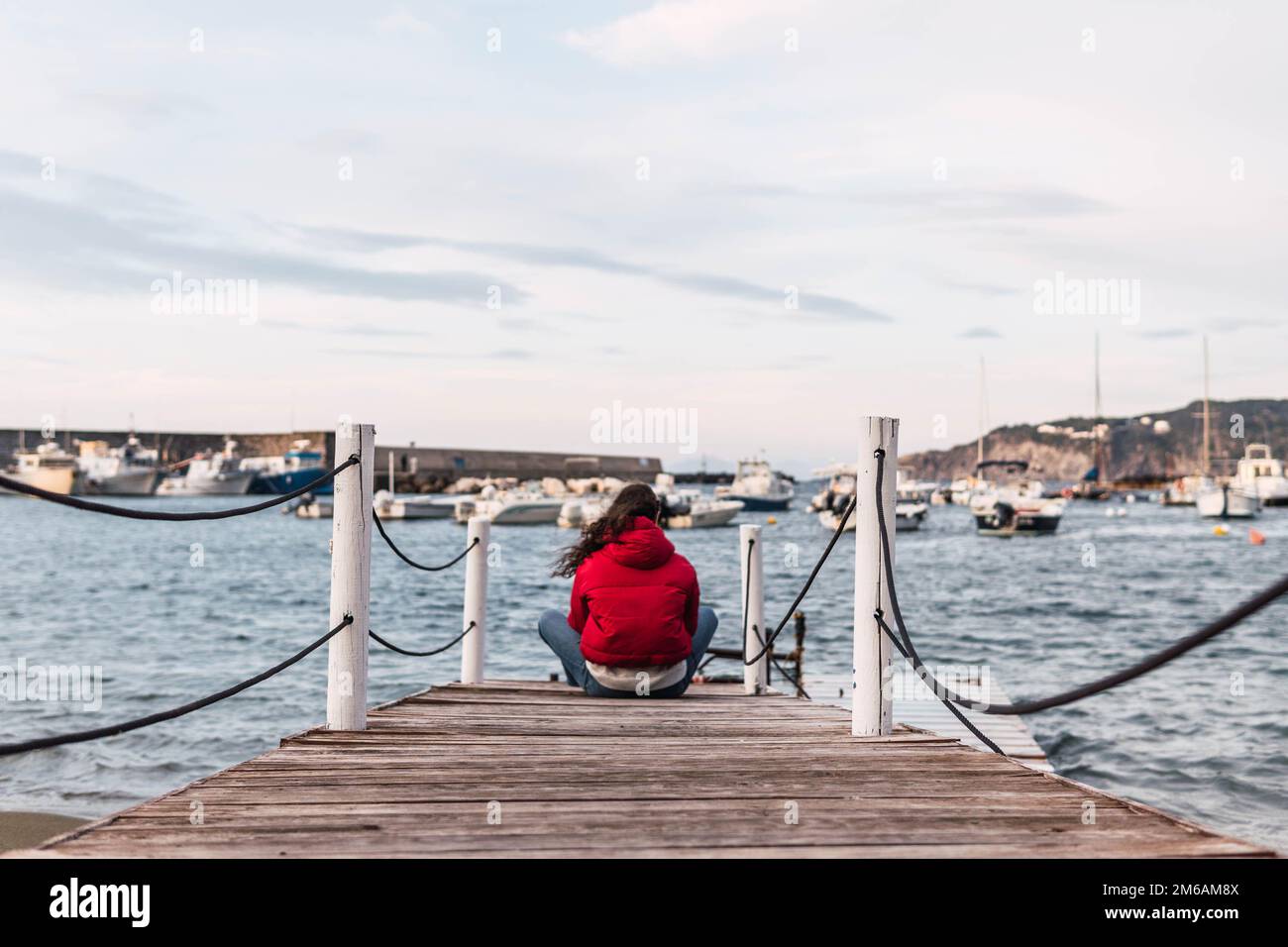Eine Frau, die auf dem hölzernen Pier vor dem Meer sitzt Stockfoto