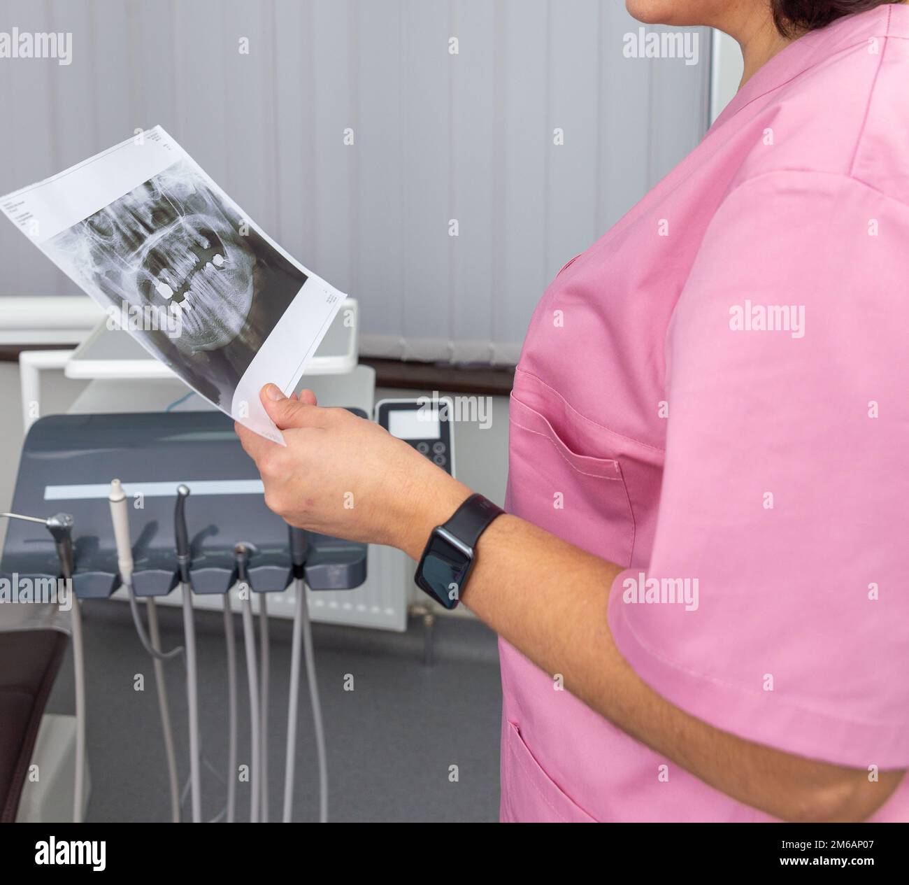 Zahnärztin in rosa Uniform, die auf das Röntgenbild des menschlichen Kiefers schaut. Beratung. Röntgenaufnahmen von Dantistin mit Zähnen. Stockfoto