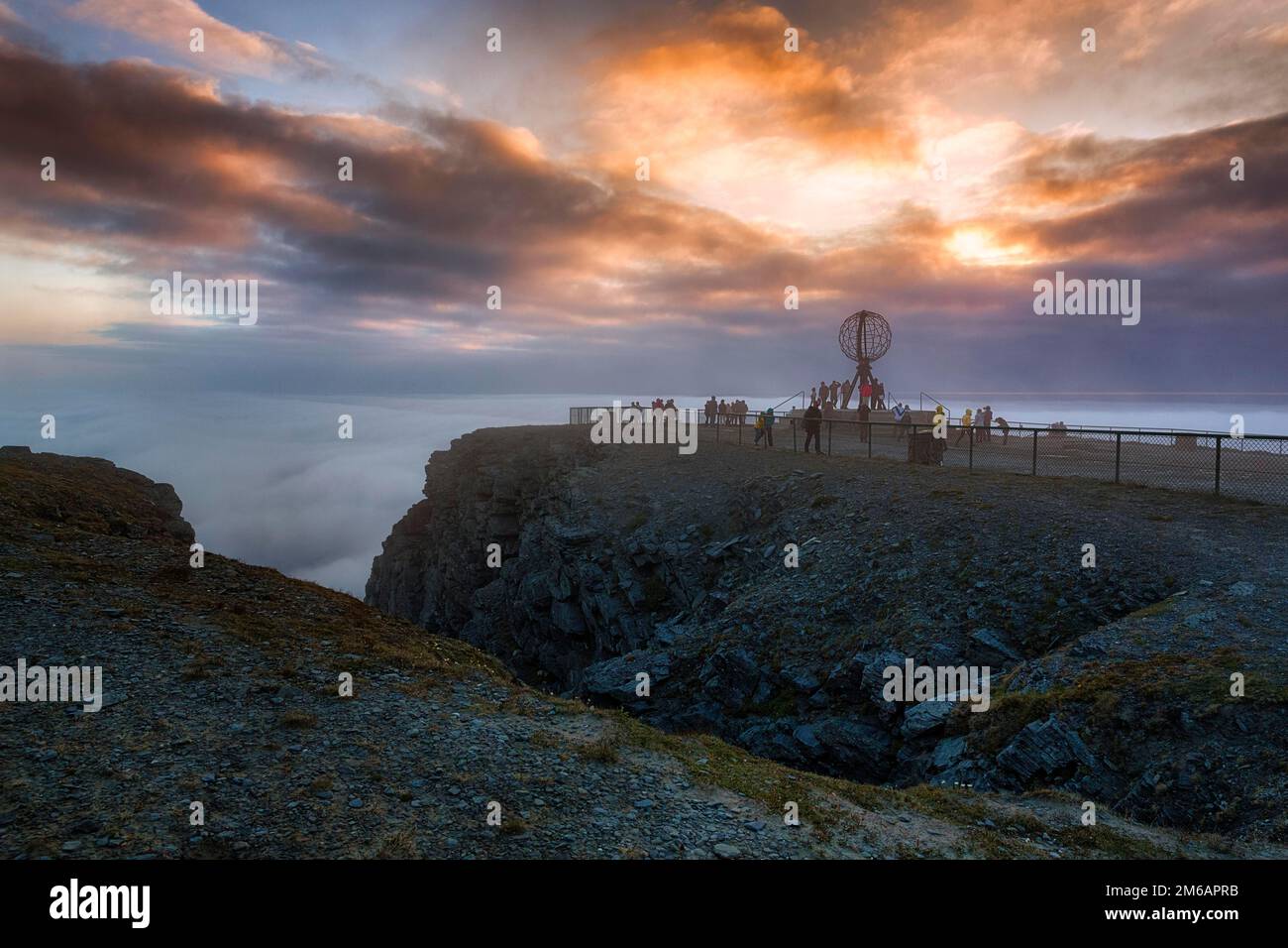 Blick vom Besucherzentrum auf die felsige Küste und Besucherplattform mit Globus, Mitternachtssonne hinter Wolken, Nordkap bei Nacht, Nordkapp, Mageroya Stockfoto