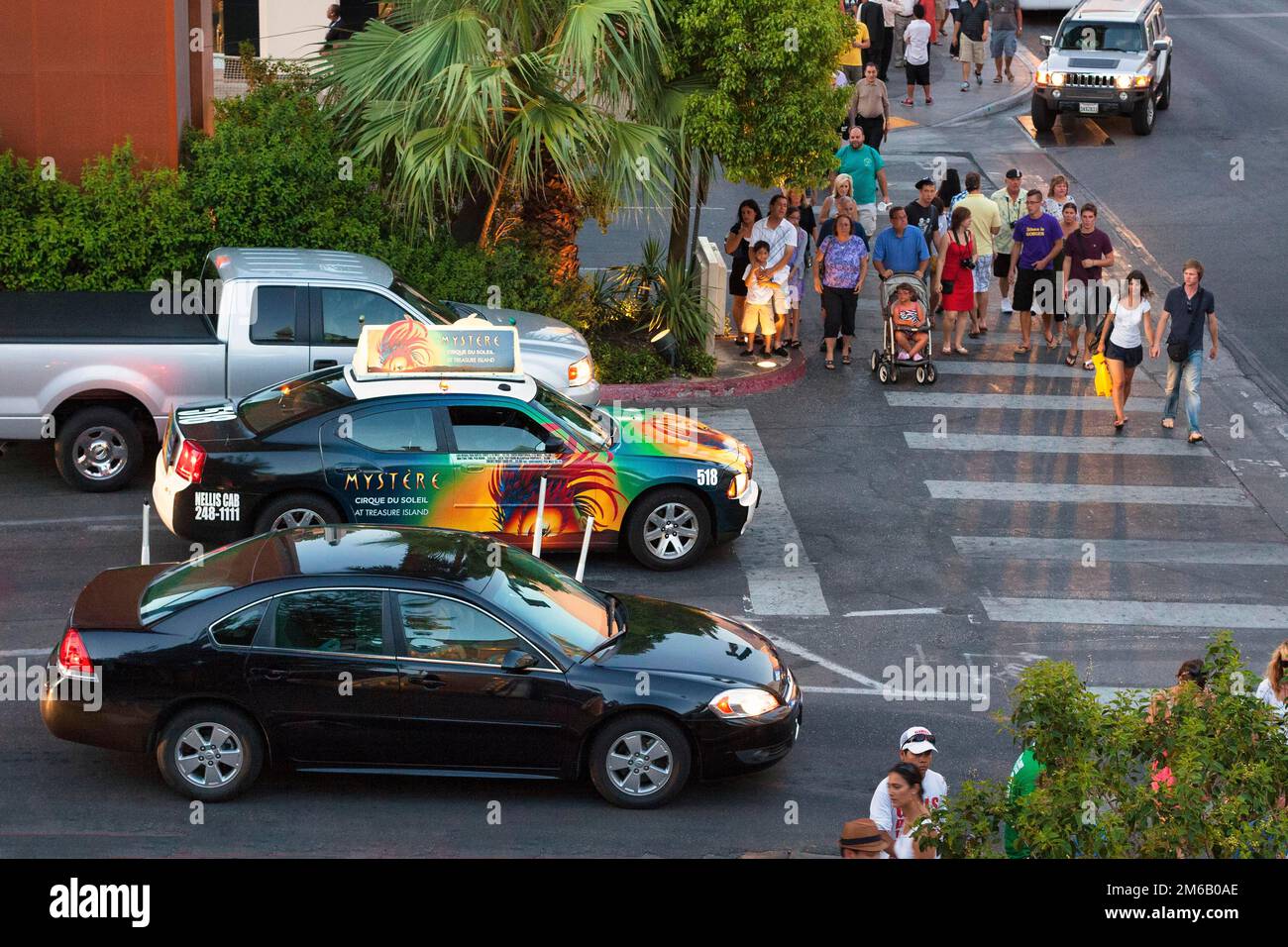 Auto und Taxi mit farbenfroher Werbung an einer belebten Kreuzung, Fußgänger, die über Zebraübergänge laufen, Blick von oben, Dämmerung auf Las Vegas Stockfoto