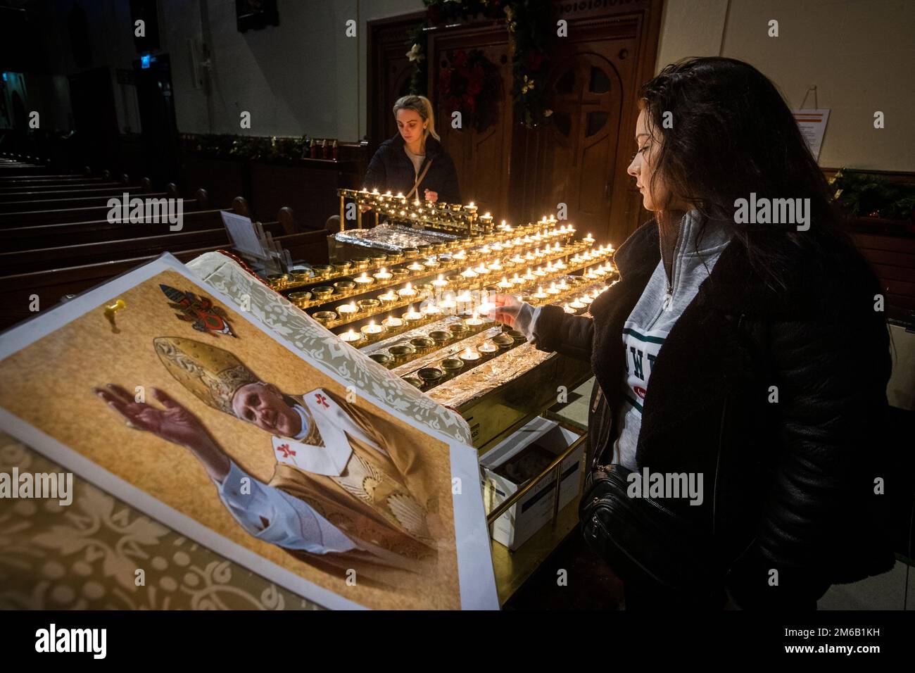 Lucy Knowles (rechts) und ihre Cousine Amie Doak zünden Kerzen neben einem Bild von Papst Emeritus Benedict XVI. In der St. Mary's Church in Belfast, Nordirland an. Benedict, 95, starb am Samstag nach 10 Jahren in einer außergewöhnlichen päpstlichen Pensionierung in einem Kloster im Vatikanischen Garten. Foto: Dienstag, 3. Januar 2023. Stockfoto