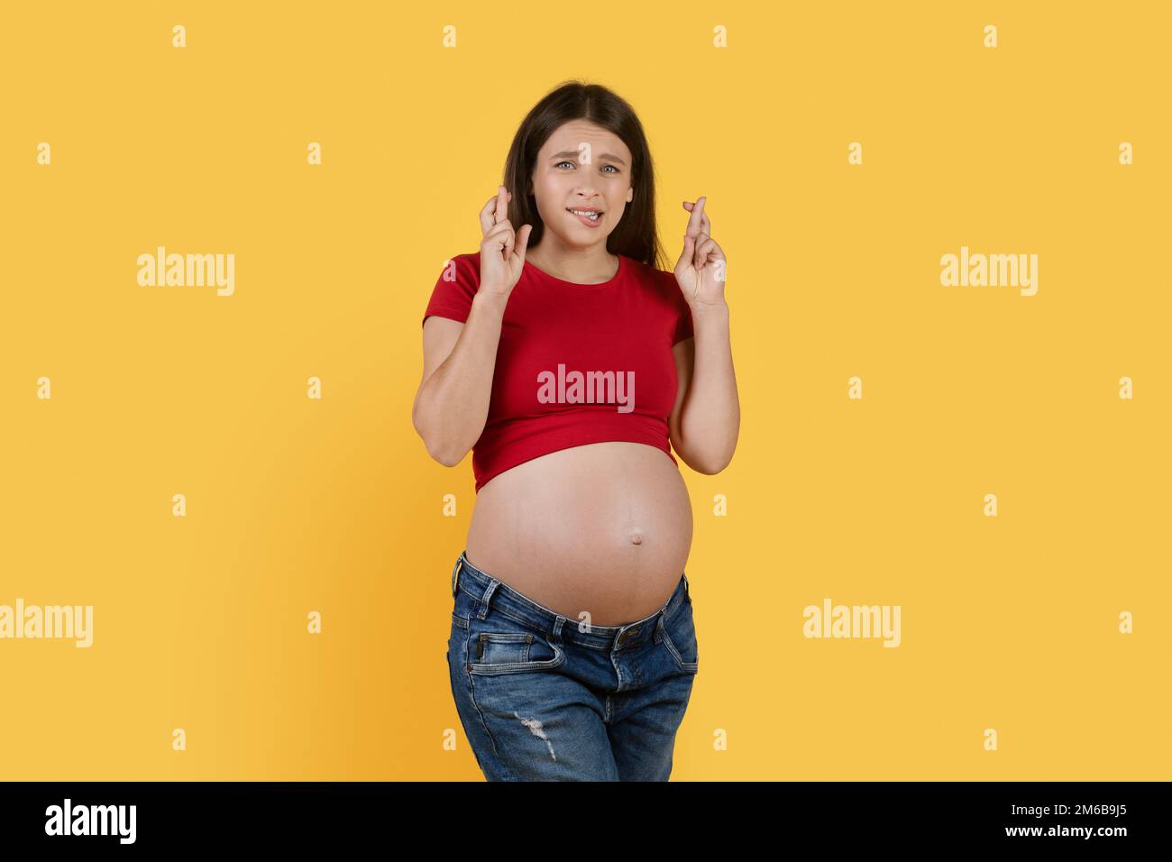 Schwangere Frau, Die Sich Mit Gedrückten Fingern Über Dem Hintergrund Des Yellow Studio Wünscht Stockfoto