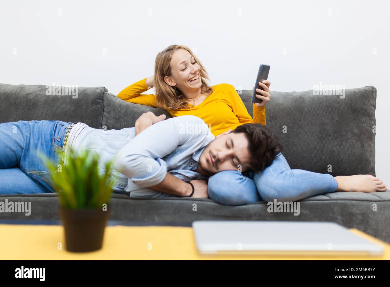 Ein Junge, der ein Nickerchen auf dem Schoß seiner Freundin macht, während sie auf ein Smartphone schaut und lächelt. Stockfoto