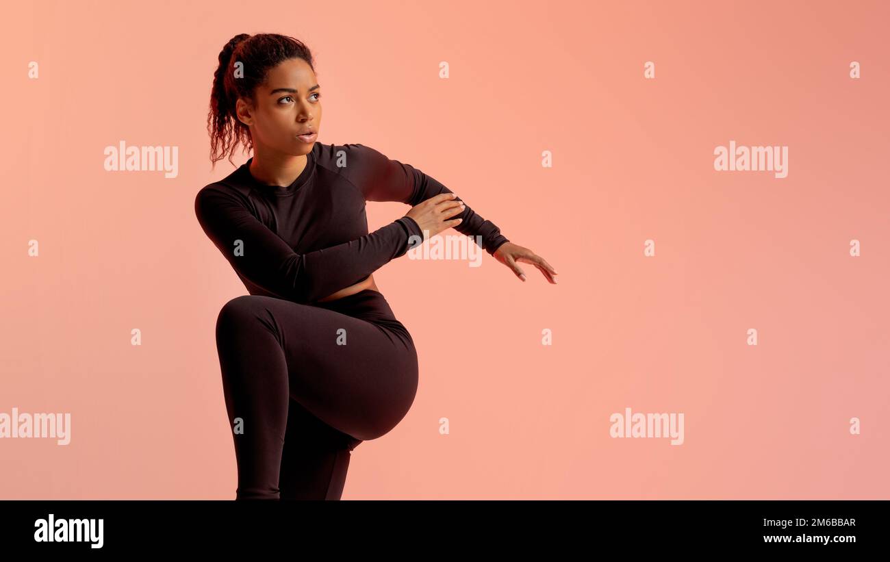 Fitness-Schwarze Frau, die den Ellenbogen bis zum Knie drückt, auf freien Platz schaut, Neon-Pfirsich-Hintergrund, Panorama Stockfoto