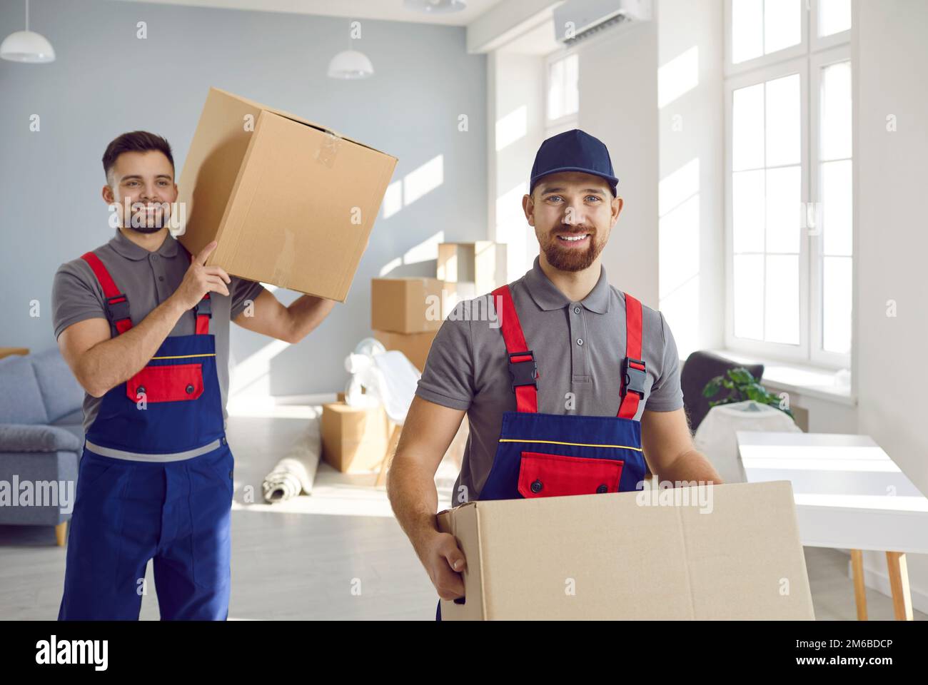 Zwei lächelnde Deledereimänner oder Transportarbeiter tragen Pappkartons, um in die Wohnung zu ziehen. Stockfoto