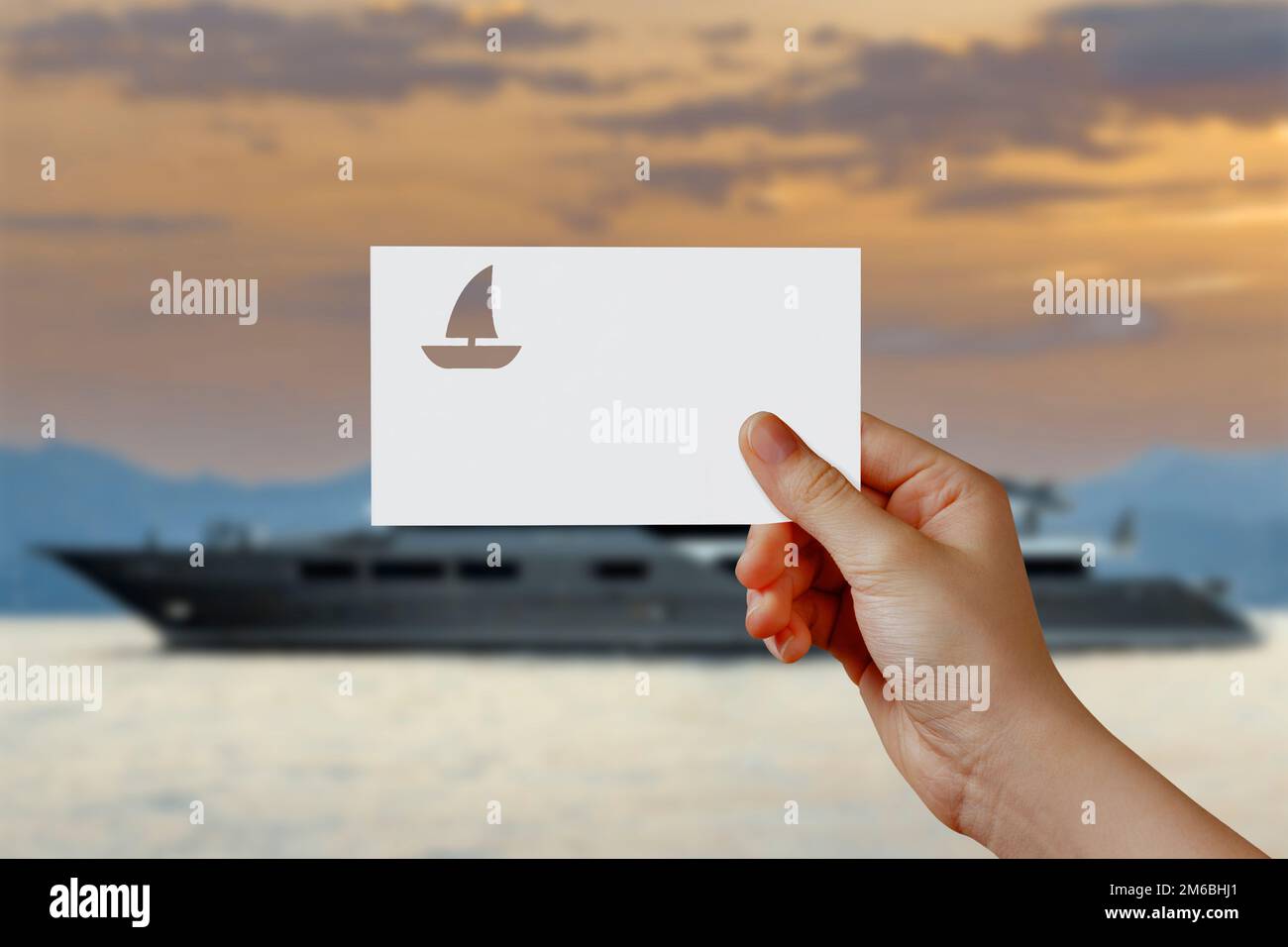 Die Hand eines Mannes, der das Yachtsymbol vor dem Meer hält. Konzept von Reise, Reise, Traum, Freiheit. Hand hält Papierboot gegen Yachtstation wi Stockfoto