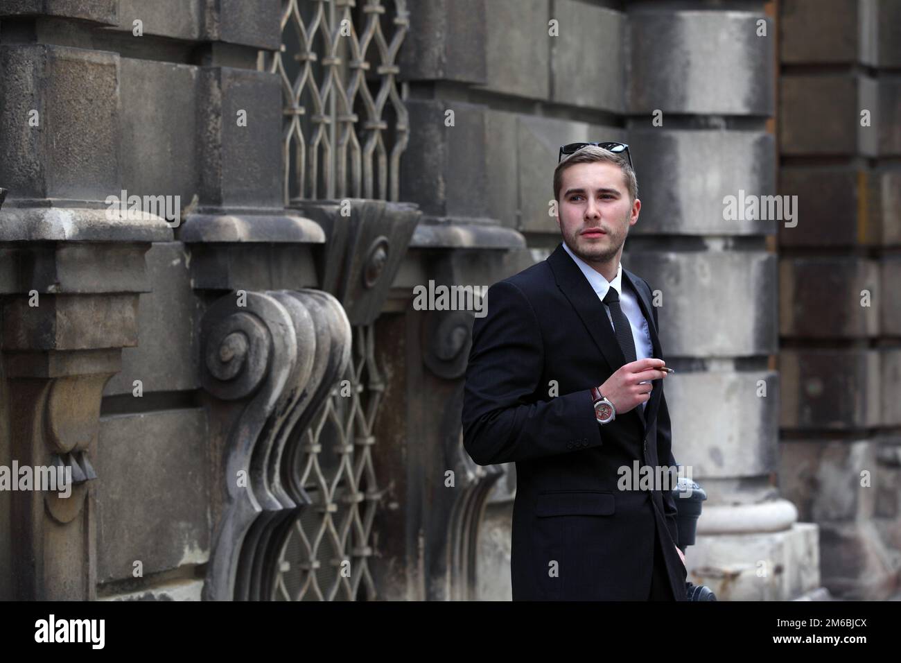 Hübscher junger Mann im schwarzen Anzug, der auf der Straße eine Zigarre raucht Stockfoto