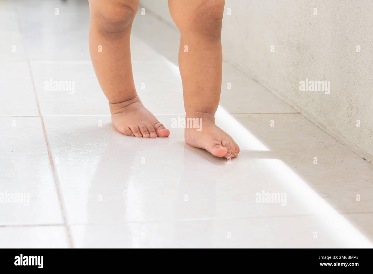 Die ersten Schritte eines Latina-Babys, das auf einem weißen gefliesten Hintergrund laufen lernt Stockfoto