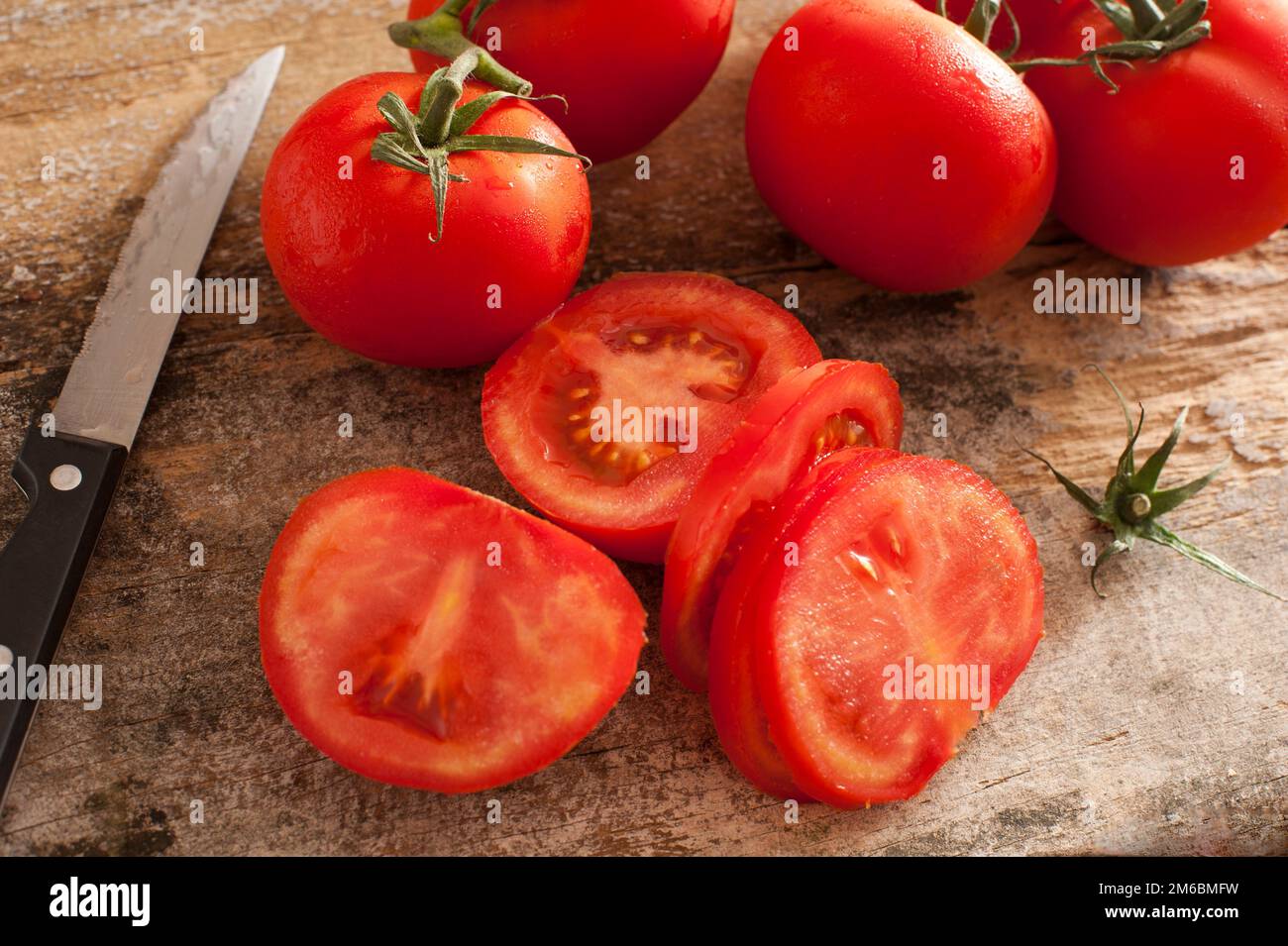 Geschnittene saftige rote Tomaten neben dem gezackten Messer Stockfoto