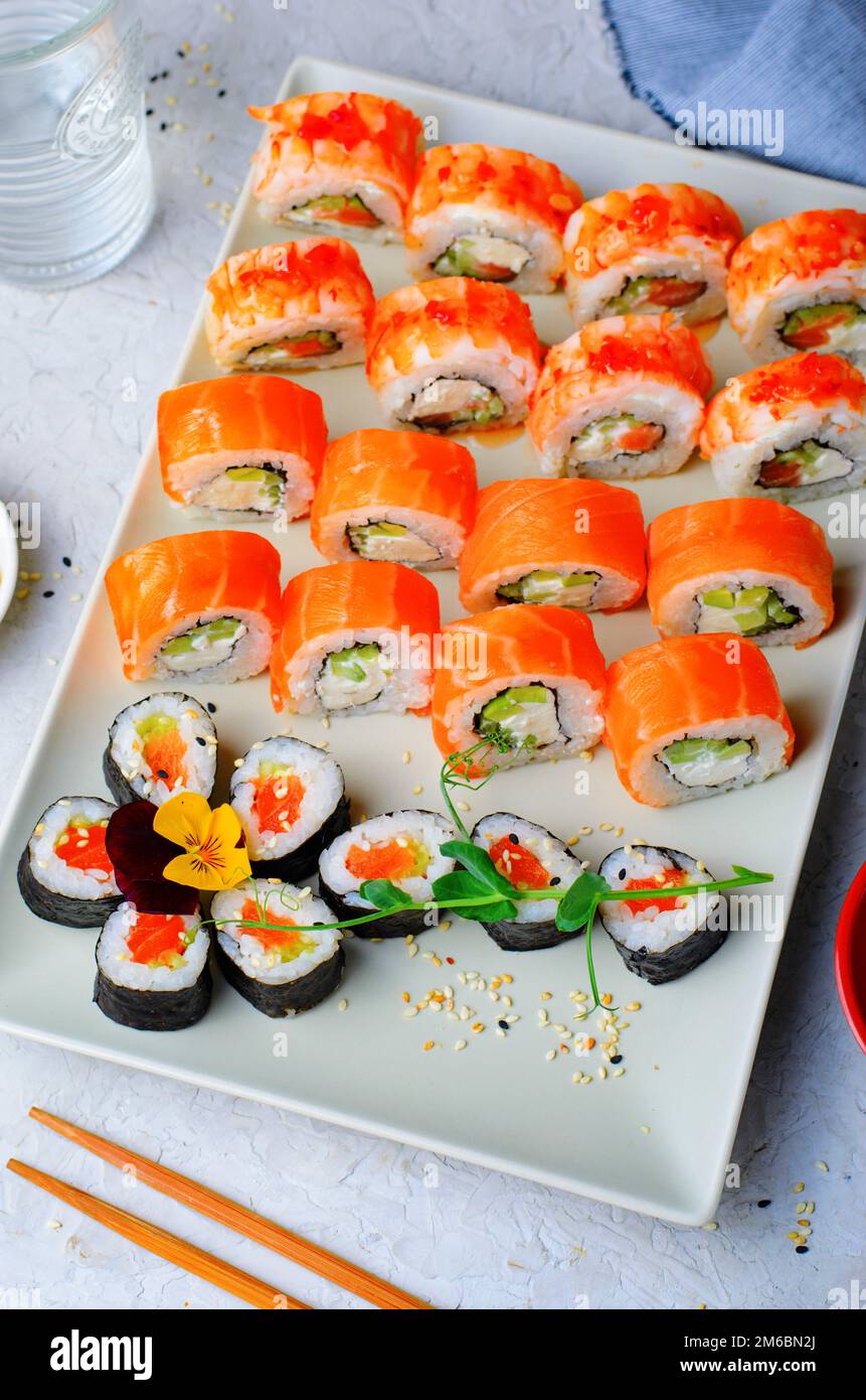 Sushi-Brötchen mit Lachs und Garnelen auf hellblauem Hintergrund, blumige Maki Sushi Rolls, japanische Küche Stockfoto