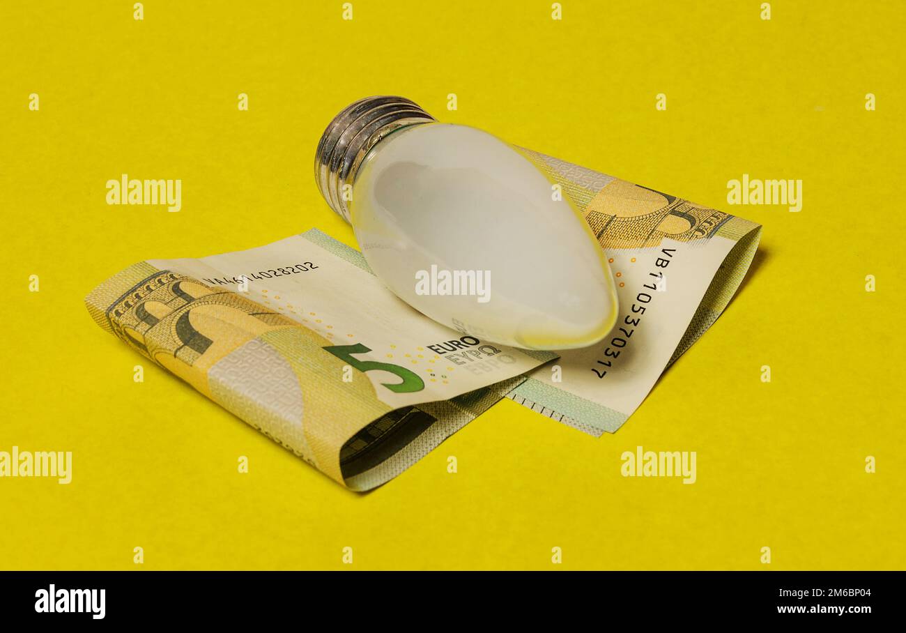 Die elektrische Glühlampe und Euro-Noten auf gelbem Hintergrund Stockfoto