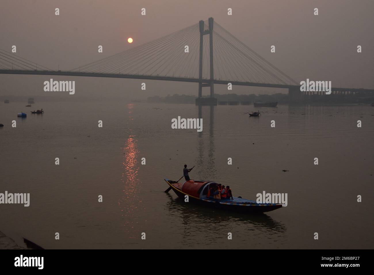 31. Dezember 2022, Kalkutta, Indien. Die Menschen fahren in ihren Booten während des Sonnenuntergangs über die Howrah Bridge (Vidyasagar Setu) auf dem Ganges. Malerische Schönheit der untergehenden Sonne am letzten Tag des gregorianischen Kalenderjahres 2022, am 31. Dezember 2022, in Kalkutta, Indien. (Kreditbild: © Biswarup Ganguly/Eyepix via ZUMA Press Wire) Stockfoto