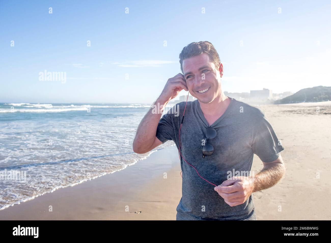 Mann am Strand mit Ohrhörern Stockfoto