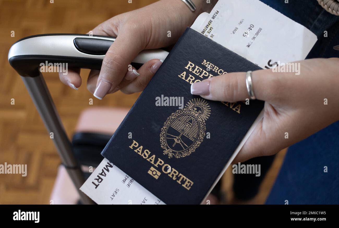 Junge Frau, die den argentinischen Pass mit ihren Reisetaschen zeigt. Übersetzung: "Pasaporte" bedeutet "Passport". "Mercosur: República Argentinien" bedeutet Mercosur Stockfoto
