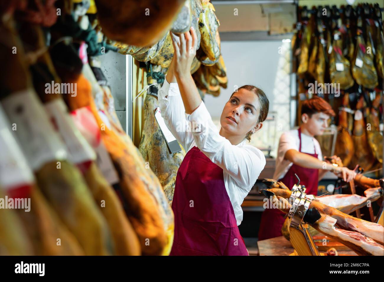 Junge Verkäuferin, die an der Theke des Metzgers arbeitet und iberischen Jamon verkauft Stockfoto