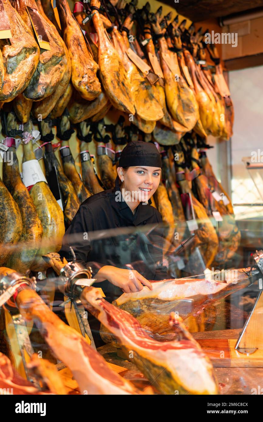 Weibliche Verkäuferin schneidet Scheiben aus dem ganzen Schenkel des Jamons im Fleischladen Stockfoto