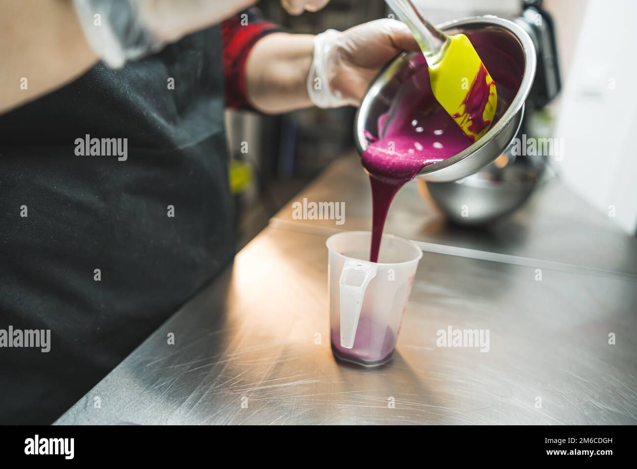 Gebäck dekorieren. Der Konditor präsentiert zubereitetes, geschmolzenes rosa Glasur aus einer Schüssel in eine Tasse. Professionelle Küche. Hochwertiges Foto Stockfoto