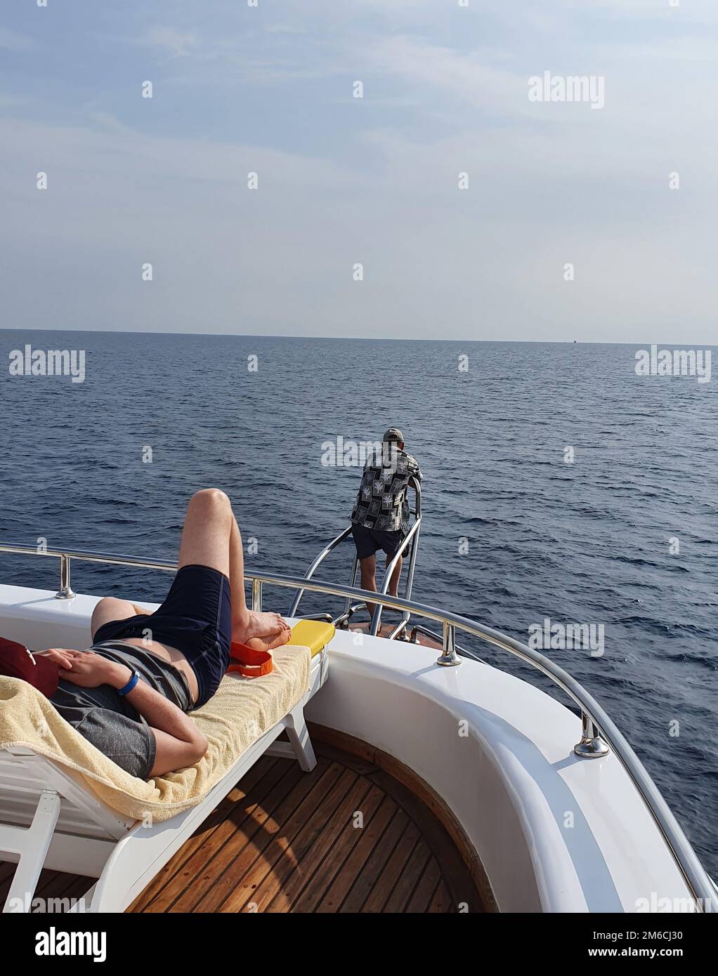 Ein Mann auf einer Sonnenliege verbringt einen Urlaub auf einer Jacht und schaut auf das Meer Stockfoto