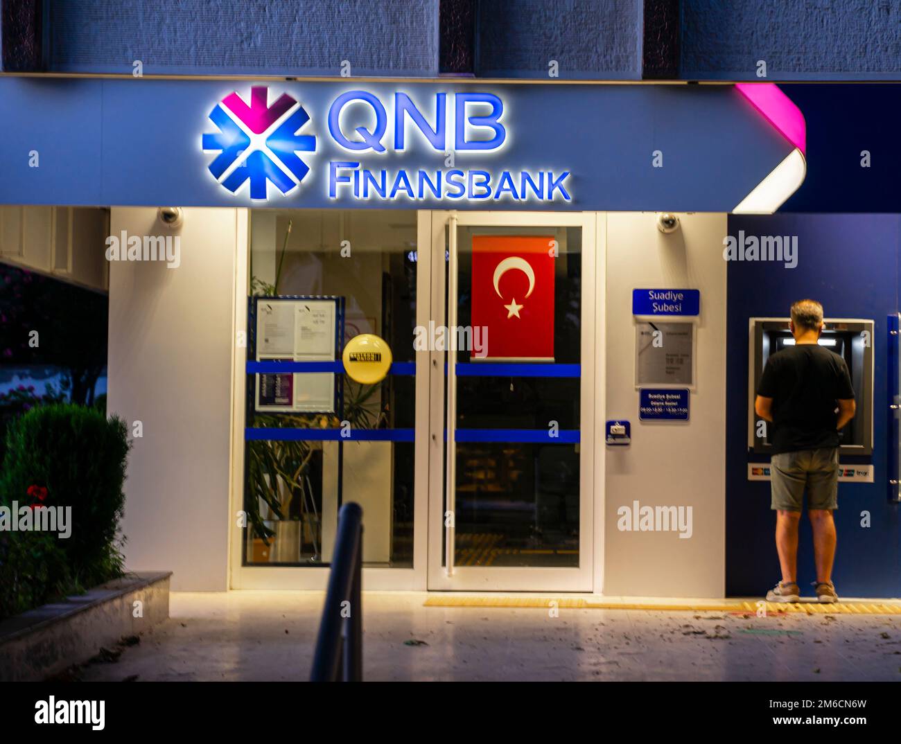 Turkish Banks - QNB Finansbank - farbenfrohe, beleuchtete Bankgebäude. Kadikoy Istanbul Türkei. Junger Mann, der Geld am Geldautomaten abhebt Stockfoto