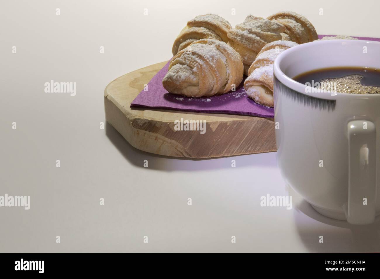 Süße Brötchen auf einer violetten Serviette, eine Tasse Kaffee, ein Holzständer, weißer Hintergrund. Stockfoto