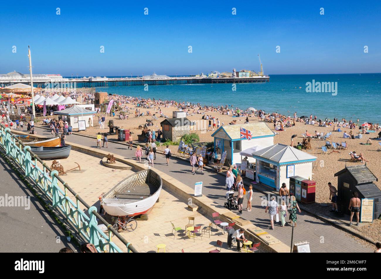 Blick auf das sonnige Sommerwetter auf der Brighton Seafront Promenade und dem Strand mit Palace Pier im Hintergrund, East Sussex, England, Großbritannien Stockfoto