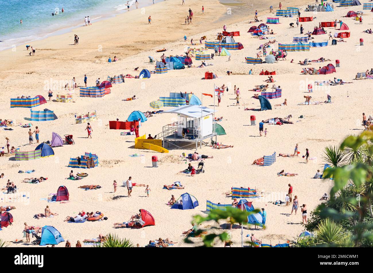Urlauber und Touristen sonnen sich und genießen das Sommerwetter am Porthminster Beach mit RNLI Lifeguard Hut im Zentrum, St Ives, Cornwall, Großbritannien. Stockfoto