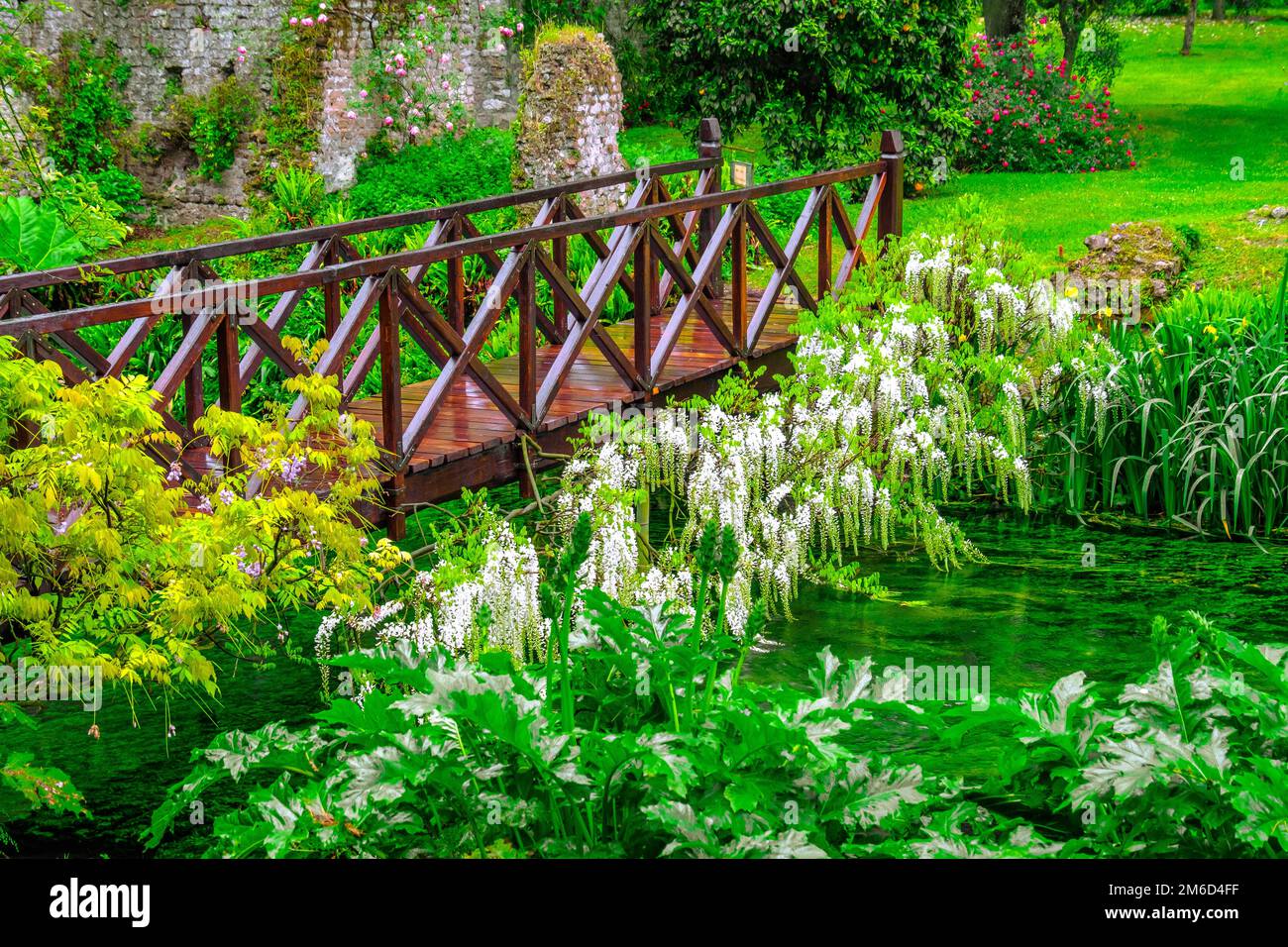 Märchenhafte Brücke lebendig grüner Fluss Holz voller Blumen im Ziergarten Stockfoto