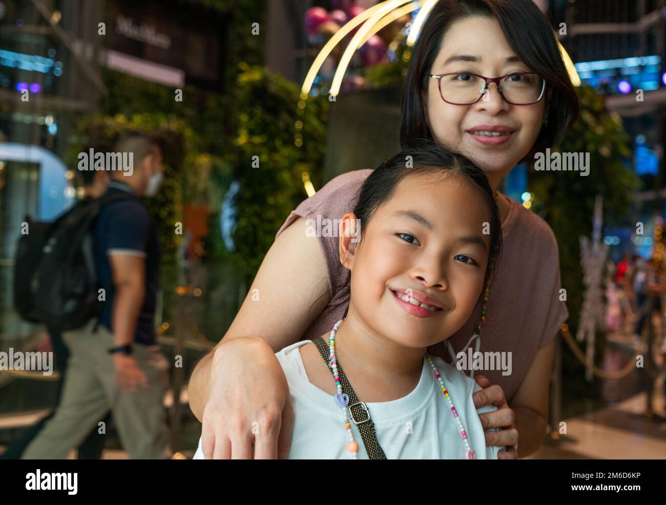 Porträt asiatische Touristenmutter und kleine Tochter in einem Einkaufszentrum in Bangkok, Thailand. Konzentrieren Sie sich auf das Kind, lächelndes Gesicht, verschwommener Hintergrund des Stockfoto