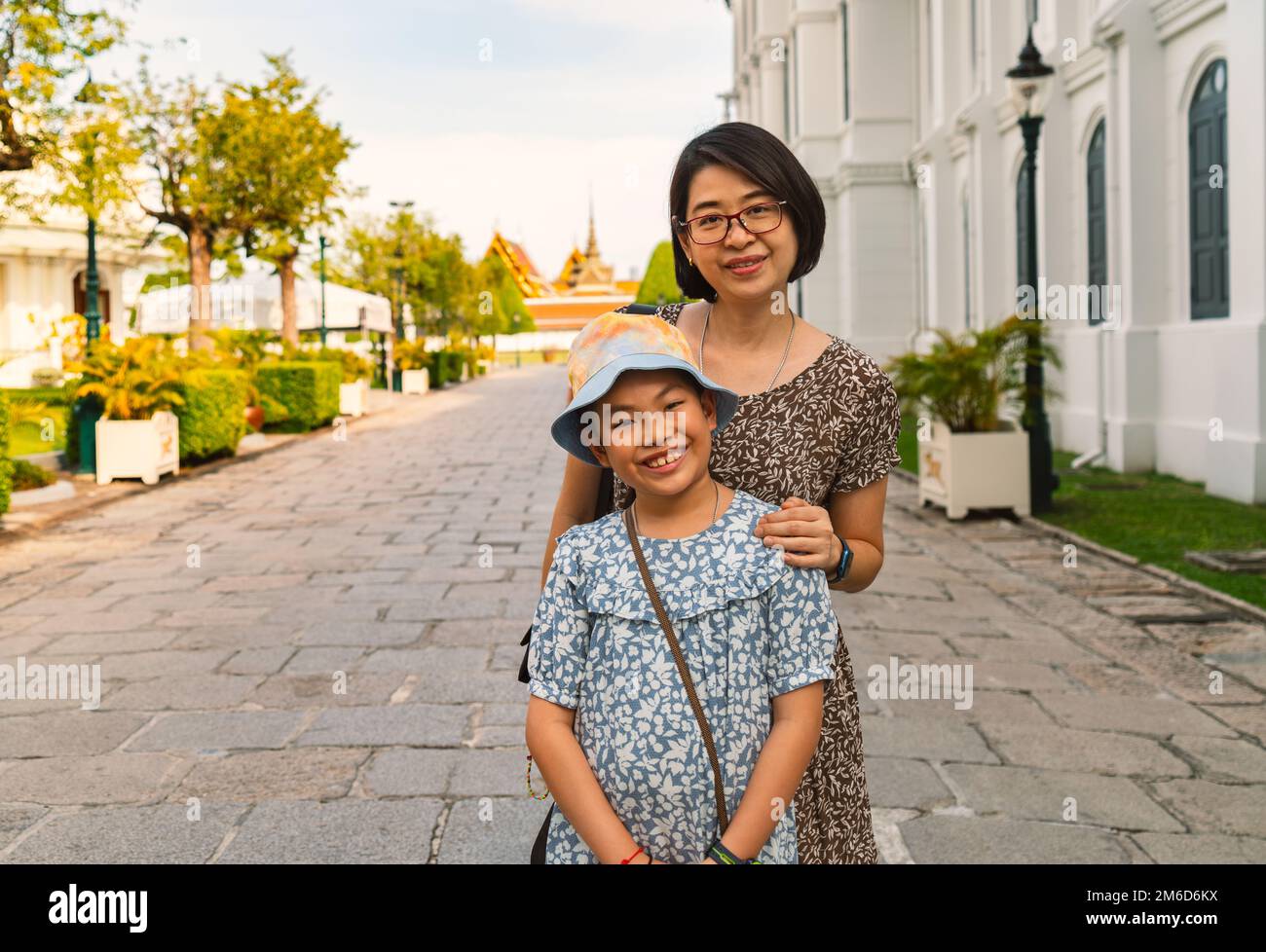 Porträt asiatische Touristenmutter und kleine Tochter im Großen Palast von Thailand, trägt höfliches Kleid, fröhliche Momente zusammen, lächelndes Gesicht, guckt Stockfoto